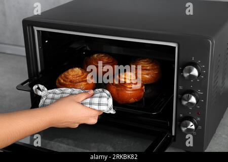 Primo piano: Donna che toglie la teglia da forno con deliziosi panini a spirale dal forno elettrico Foto Stock