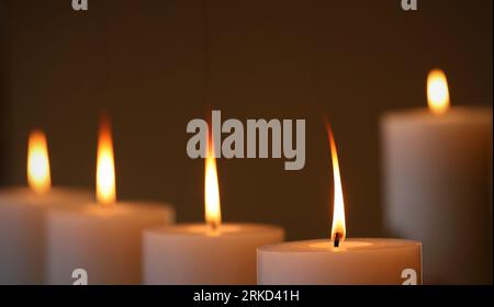 5 grandi candele di cera bianca che bruciano con lunghe fiamme gialle arancioni. Disposizione a cinque candele con sfondo scuro. Foto Stock