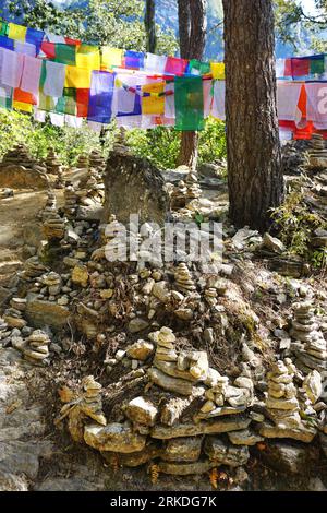 i cairn in pietra impilati riempiono il primo piano, mentre le colorate bandiere di preghiera fanno da sfondo lungo l'aspro sentiero fino al monastero del Nido della Tigre del Bhutan Foto Stock