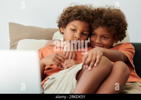 Fratelli che si coccolano sul letto e guardano film sul computer portatile Foto Stock