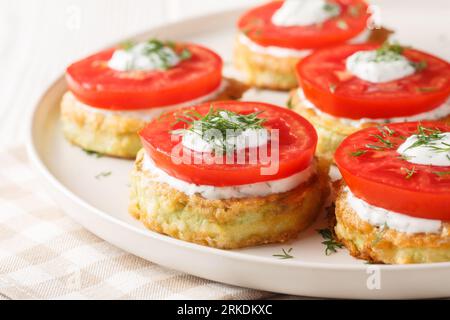 Le zucchine fritte in pastella vengono servite con pomodoro fresco e salsa cremosa da vicino in un piatto sul tavolo. Orizzontale Foto Stock