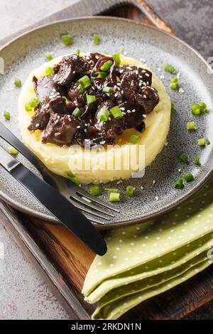 Chicken liver with onions stewed in honey wine sauce with garnish mashed potatoes close-up in a plate on the table. Vertical Stock Photo