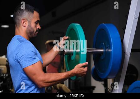 Forte uomo ispanico che mette il piatto di peso sul campanello in palestra. Foto Stock