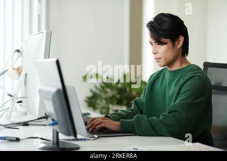 Ritratto di un uomo asiatico serio che codifica su un computer portatile alla sua scrivania Foto Stock