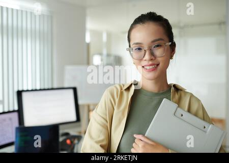 Ritratto della giovane e gioiosa sviluppatrice di software che si trova sul suo nuovo posto di lavoro Foto Stock