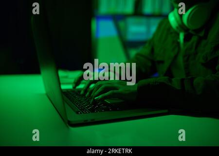 Hacker che lavora su un computer portatile in una stanza d'ufficio verde al neon Foto Stock