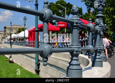 ringhiera in ghisa grigia lungo il marciapiede pubblico in asfalto. passaggio di pedoni sfocati. base in pietra. Scena estiva sulla famosa strada urbana di Budapest Foto Stock