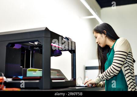 Vista laterale di una donna d'affari che utilizza un computer portatile con stampante 3D sul tavolo in ufficio Foto Stock