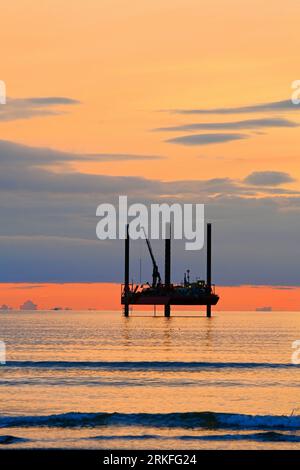 Carro di prova di perforazione con nuvole all'orizzonte dorate al largo della costa del Northumberland Mare del Nord all'alba con cielo e mare dall'aspetto caldo Foto Stock