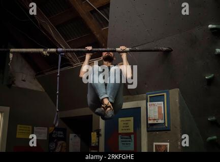 Un uomo forte che fa tira su una barra vicino a una parete per arrampicata Foto Stock