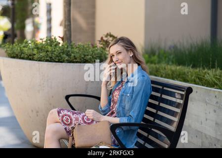 Giovane donna seduta sulla panchina che parla al telefono Foto Stock