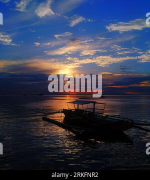 Una barca a vela è sagomata sullo splendido cielo arancione e giallo al tramonto Foto Stock