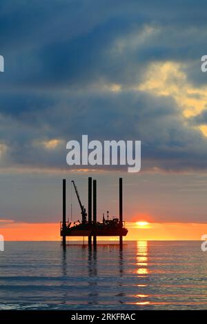 Carro di prova di perforazione con nuvole di orizzonte dorate e cielo arancione e sole appena sopra l'orizzonte al largo del Mare del Nord all'alba con cielo e mare dall'aspetto caldo Foto Stock