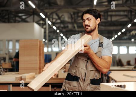 Giovane falegname che guarda e sceglie la tavola di legno in officina in una fabbrica di legno falegname Foto Stock