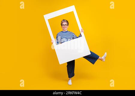 Foto a lunghezza intera di felicissima signora che indossa abiti alla moda divertiti a scattare foto isolate su sfondo giallo Foto Stock