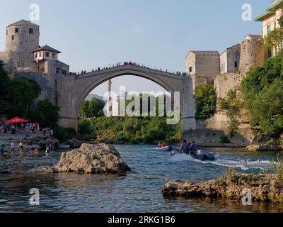 Spiaggia accanto al fiume Neretva e turisti a Stari Most (Ponte Vecchio) e alla Moschea Koski-Mehmed Pasha. Mostar, Bosnia ed Erzegovina, 20 agosto 2023. Foto Stock