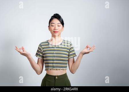 Attraente donna asiatica raccoglie coraggio pazienza respirare aria chiudere gli occhi tenere le mani zen mudra gesto Foto Stock