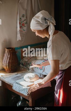 Il processo di cottura tradizionale del pane a casa. Una donna in abito nazionale ucraino prepara il pane. Foto Stock