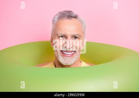 Photo of cheerful friendly man with beard dressed yellow t-shirt smiling from inflatable lifesaver isolated on pink color background Stock Photo