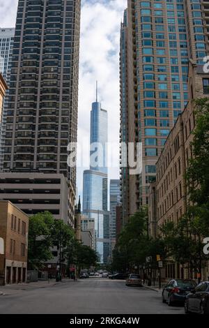 Una fila di auto parcheggiate lungo il marciapiede di una strada cittadina di fronte a un torreggiante skyline di grattacieli Foto Stock