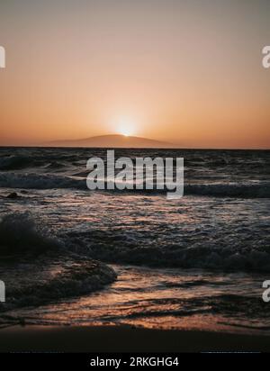 Una pittoresca scena al crepuscolo di una spiaggia sabbiosa con onde dolci che si infrangono sulla riva Foto Stock