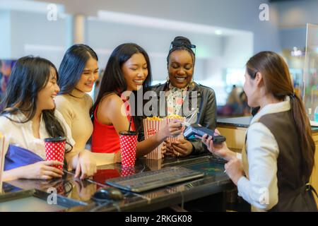Le amiche interrazziali pagano i biglietti del film con una carta di credito al bancone, offrendo la comodità senza contatto per un ci senza interruzioni Foto Stock
