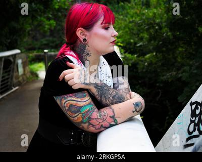 Donna di vent'anni con capelli rossi tinti e tatuaggi appoggiati su una passerella metallica a Leeds, West Yorkshire, Inghilterra Foto Stock