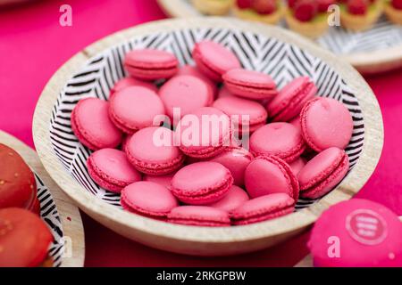 Un assortimento di macaron e biscotti rosa in una ciotola di ceramica, esposti su un tavolo di legno Foto Stock