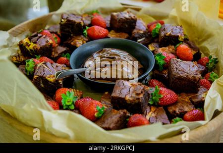A close-up shot of a ceramic bowl full of freshly-baked brownies, topped with strawberries and drizzled with a rich chocolate ganache Foto Stock