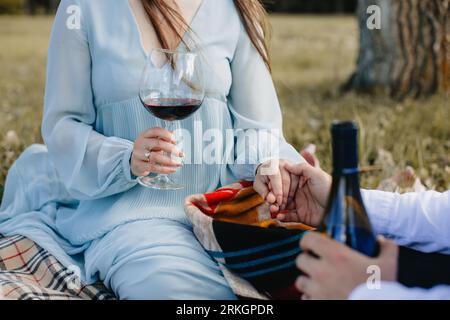 Una coppia amorevole si gode una serata romantica insieme, con la donna che tiene un bicchiere di vino in una mano e la mano del suo partner nell'altra Foto Stock
