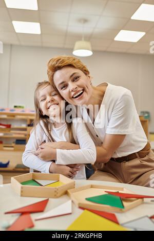 insegnante positivo che abbraccia allievo vicino al materiale didattico della scuola montessori Foto Stock