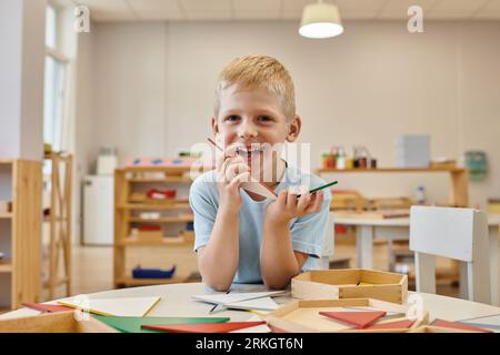 cheerful boy holding triangles during game in classroom in montessori school Stock Photo
