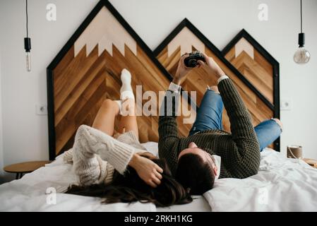 Una giovane coppia sdraiata a letto e felice di scattare selfie con una fotocamera sorridente Foto Stock