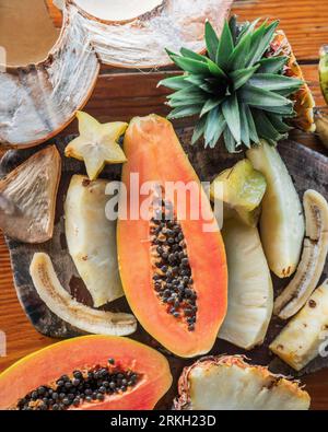 A white porcelain bowl filled with a variety of colorful fruit, such as papaya, sits atop a wooden cutting board Stock Photo