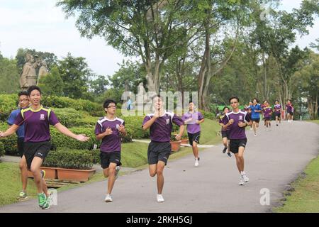 Un gruppo di persone che fa jogging lungo una strada asfaltata circondata da una lussureggiante vegetazione verde Foto Stock