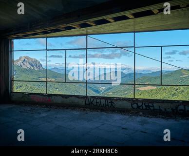 paesaggio montano visto attraverso una finestra, edificio in rovina con una finestra senza vetro che si affaccia su una valle di montagna con alte cime e nuvole Foto Stock