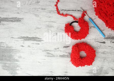 Spille a uncinetto fatte a mano in filato rosso peloso su fondo di legno bianco. Anelli elastici neri con spazio per il testo. Foto Stock