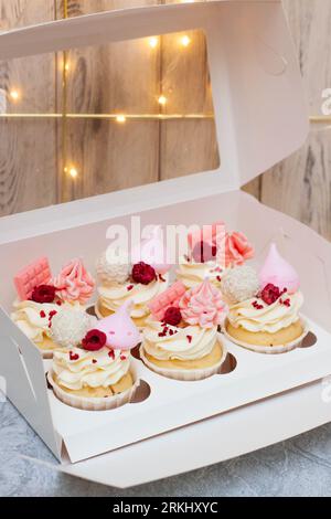 Confezione regalo con bellissimi cupcake rosa decorati con tavolette di cioccolato, meringa, glassa di lamponi e formaggio spalmabile Foto Stock