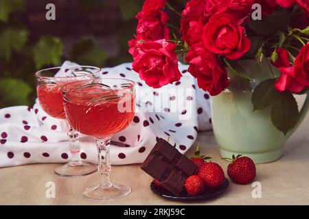 Bicchieri di vino rosso frizzante alla fragola con rose all'aperto, fragole e cioccolato. Impostazioni estetiche dei tavoli estivi. Romantico, prezioso momento conc Foto Stock