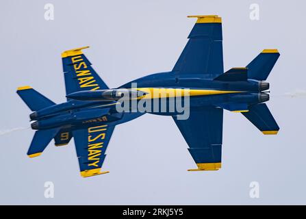 A bright blue and yellow aircraft is soaring through the sky, leaving a white smoke trail in its wake Stock Photo