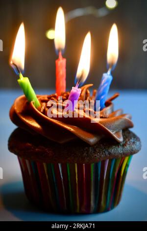 Cupcake al cioccolato con quattro candele di compleanno illuminate colorate Foto Stock