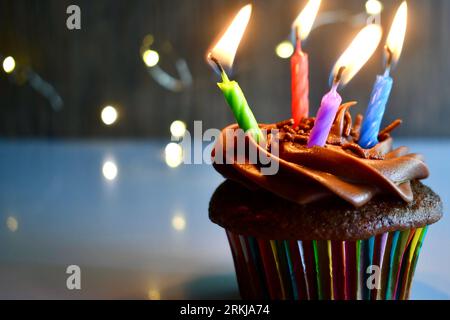 Cupcake al cioccolato con quattro candele di compleanno illuminate colorate Foto Stock