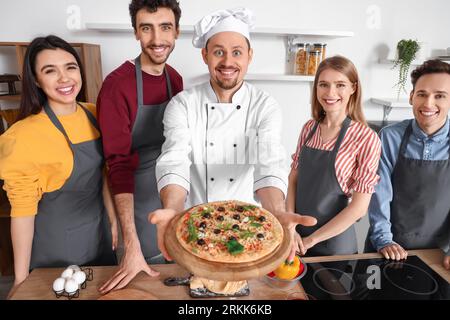 Italian chef with prepared pizza and group of young people after cooking class in kitchen Stock Photo