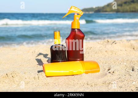 Bottiglie di crema solare sulla sabbia vicino all'oceano in spiaggia Foto Stock