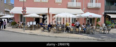 Caffetteria Café Farol, vicino alla spiaggia sabbiosa di barra con i clienti seduti a tavoli e sedie su un pavimento di ciottoli all'esterno, Aveiro, Foto Stock