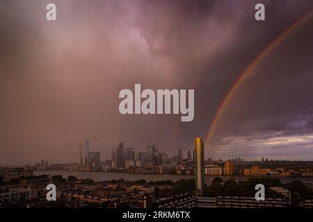 Londra, Regno Unito. 25 agosto 2023. Tempo nel Regno Unito: Un enorme arcobaleno al tramonto si ferma sugli edifici del parco commerciale di Canary Wharf nella zona est di Londra durante una breve pioggia serale. Crediti: Guy Corbishley/Alamy Live News Foto Stock