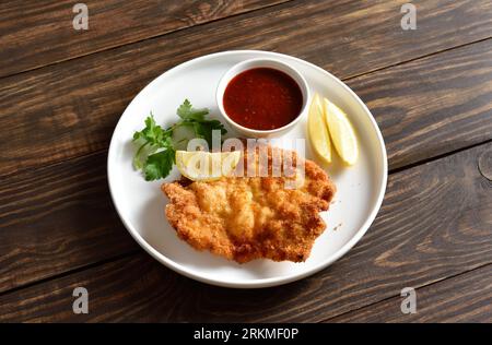 Schnitzel di maiale con salsa su piatto bianco su sfondo di legno. Vista ravvicinata Foto Stock