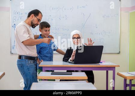 Conversazione paterna con l'insegnante a scuola su qui figlio progresso accademico Foto Stock
