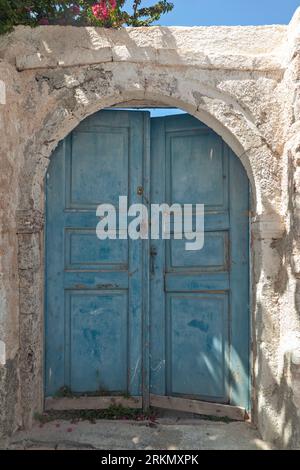 Tradizionale porta in legno di colore blu chiaro in una vecchia casa con pareti ocra e soglia di pietra, nel villaggio di Oia di Santorini, Grecia. Foto Stock