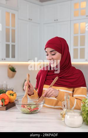 Donna musulmana che prepara una deliziosa insalata con verdure al tavolo bianco in cucina Foto Stock